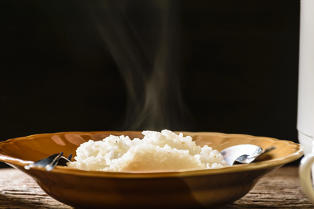 hot rice cooker with hot steam. Placed on a wooden table near the window. And the hands are scooped.の写真素材
