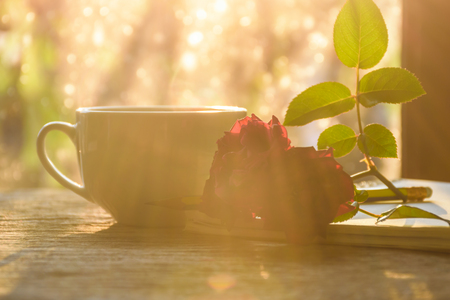 Felling warm lovely, hot cup tea , red rose , note and pencil put on old wooden table in the morning, sun ray passed window ,feeling warm heart.の写真素材