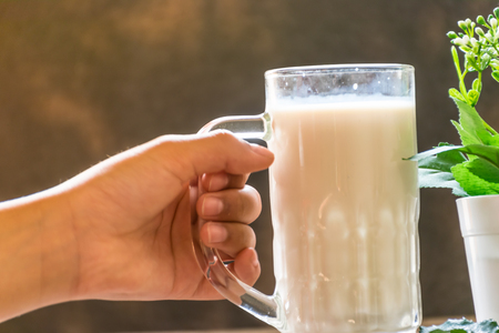 hand holding glass of milk for drinking on old wooden table, breakfast daily fresh in the morning, and orange put in side of glass. drinking to high Vitamin concept.の写真素材