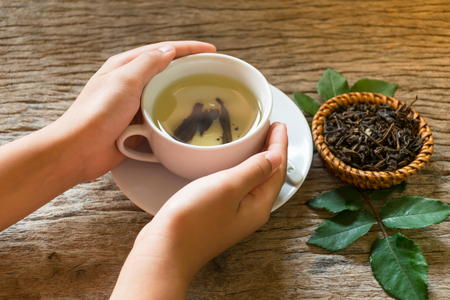 hand holding cup of tea for drinking on old wooden table, breakfast daily fresh in the morning, and orange put in side of glass. drinking to high Vitamin concept.and sun ray background.の写真素材