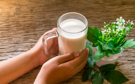 hand holding glass of milk for drinking on old wooden table, breakfast daily fresh in the morning, and flower put in side of glass. drinking to high Vitamin concept.and sun ray background.の写真素材