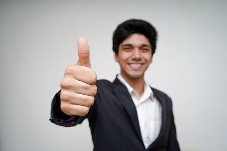 Portrait of a Young Handsome Asian Business man wearing black coat and white shirt whit selective focus on his hand,showing thumbs up and looking into the camera.の写真素材