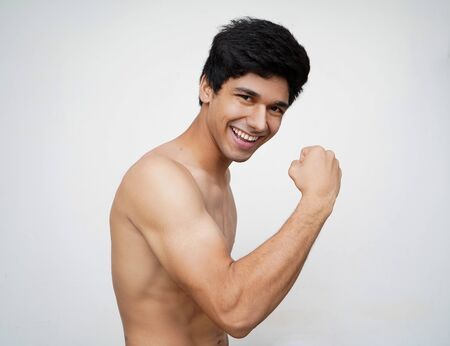 Hurray and cheers. Portrait of young handsome shirtless indian model looking excited while standing against white backgroundの写真素材