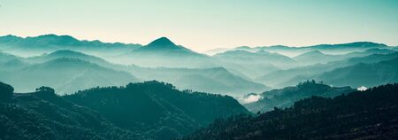 A panoramic landscape photo of mountains captured during just before sunrise, with many layers of...