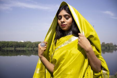 Beautiful Indian young model wearing green traditional saree standing in front of a river landscape.