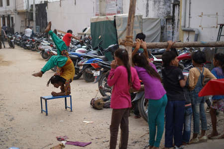 Pushkar, Rajasthan / India- June 5 2020 : A group of kids watching a poor girl doing stunts on a chair for money.のeditorial素材