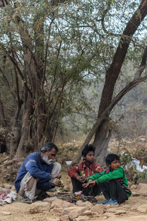 New Delhi, Delhi / India- May 31 2020: Two sons and father sitting in the middle of a forest trying to light up a fireのeditorial素材