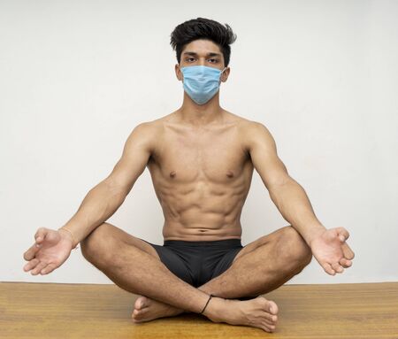 Young handsome shredded boy doing yoga wearing a blue maskの写真素材