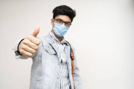 Young handsome asian college student with bag and wearing mask showing thumbs up in the camera.の写真素材