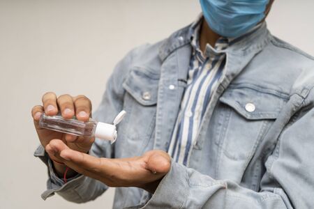 Young handsome asian boy in denims wearing a mask using a hand sanitizer.の写真素材