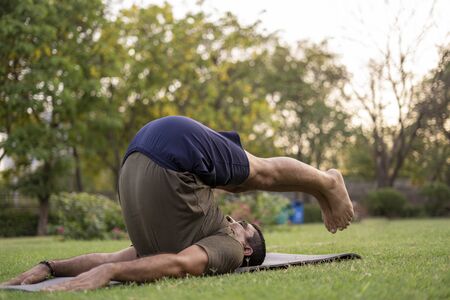 Mid-aged Man doing yoga in a park covered with trees
