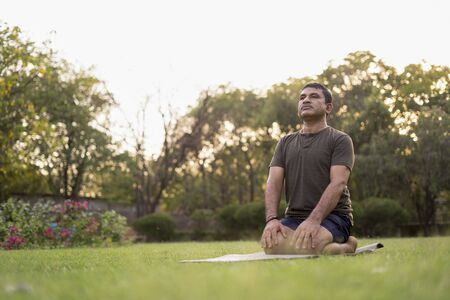 Mid-aged Man doing yoga in a park covered with trees on International Yoga Day.の写真素材