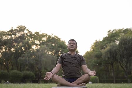 Mid-aged Man doing yoga in a park covered with trees on International Yoga Day.の写真素材