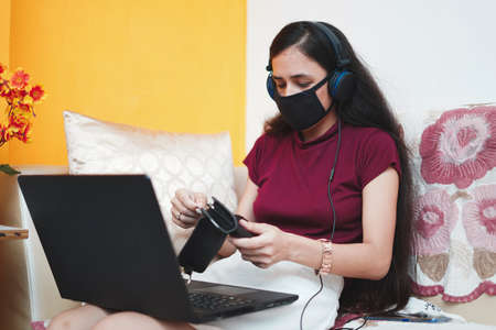 A young indian girl taking out cards from her wallet while wearing a mask on her face for protection from covid-19, work from home concept.の写真素材