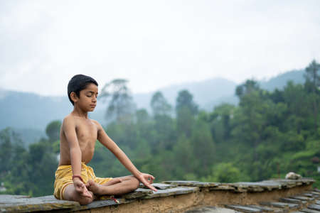 A young indian cute kid doing yoga in the mountains,wearing a dhotiの写真素材