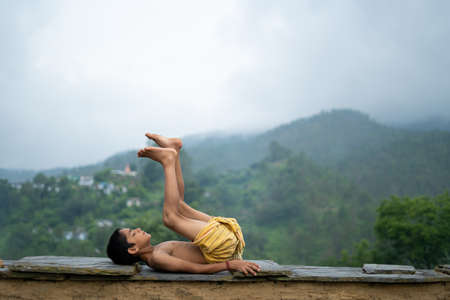 A young indian cute kid doing yoga in the mountains,wearing a dhotiの写真素材