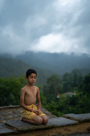 A young indian cute kid doing yoga in the mountains,wearing a dhotiの写真素材