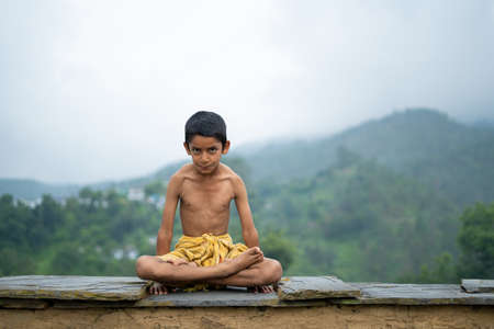 A young indian cute kid doing yoga in the mountains,wearing a dhotiの写真素材