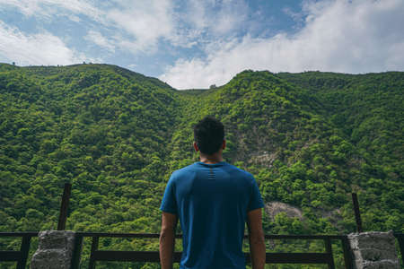 young indian boy standing in the edge of the balcony, enjoying the scenic view of the green...