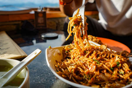 Chef picking up the Schezwan Noodles or Chiken Hakka Noodles or chow mein is a popular Indo-Chinese recipes, served in a bowl or plate with the help of spoon.の写真素材