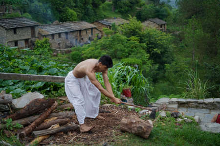 A young boy wearing a white dhoti chopping wood with an axe.の写真素材