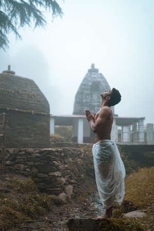 Young man with shredded body wearing dhoti, praying in the temple early in the morning.