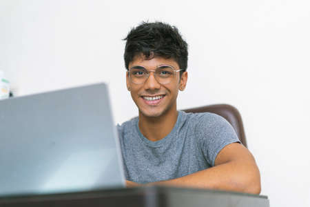 Indian teenager working on his laptop while looking into the camera.の写真素材