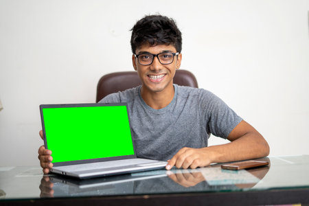 Young man working in office on his laptop, showing his laptop with green screen.の写真素材