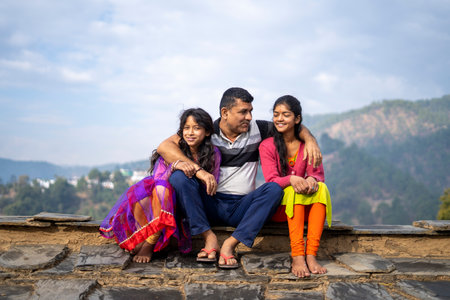 Indian father sitting with his daughters and smiling, happy family concept.の写真素材