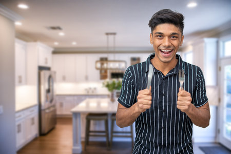 portrait of young joyful boy looks into the frame and holds a fork and a spoon.