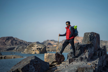 Young indian traveler standing confidently on top of the mountain over a cliff, wearing a red snow...