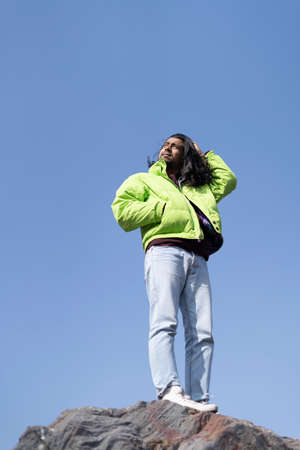 Young Indian boy standing on the top of cliff wearing a snow jacket and track pants. Enjoying and freedom concept.の写真素材