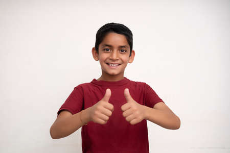 Young indian kid showing thumbs up into the camera while smiling. Small kid education concept.の写真素材