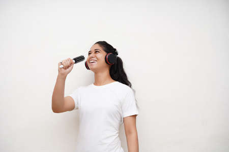 Young beautiful indian Emotional girl in pajamas singing in hairbrush on white background