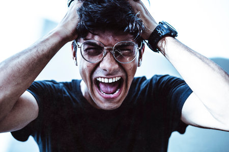 Young handsome boy wearing glasses screaming while holding his head. Depression and Anxiety Concept.