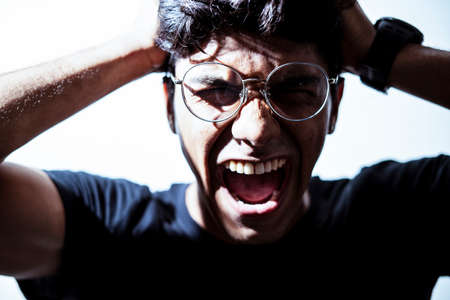 Young handsome boy wearing glasses screaming while holding his head. Depression and Anxiety Concept.の写真素材