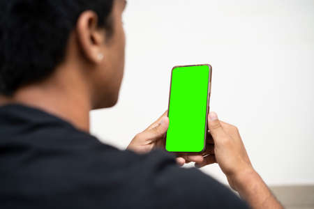 shoulder shot of a young boy working on his mobile phone with green screen on it. Mockup and...