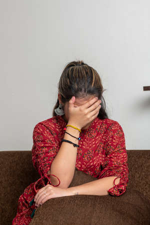 Young indian girl getting sad, covering her face because of sadness. A girl crying while sitting on the couch.の写真素材