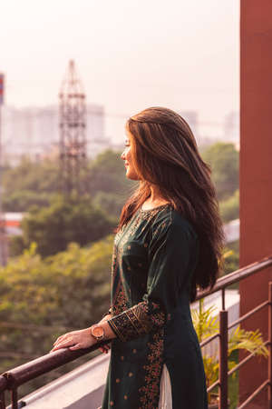 Young girl standing on her balcony during sunset, enjoying the beautiful view of the city.の写真素材