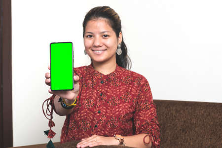 Young indian girl showing her mobile phone with green screen. Indian girl in traditional clothes with a mobile phone.の写真素材