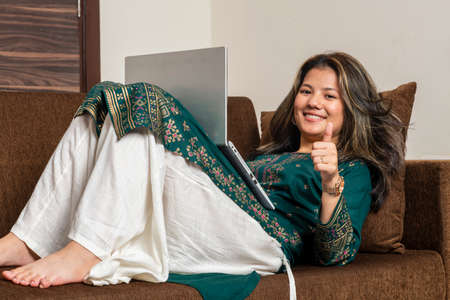 Young Indian girl showing thumbs up while looking the camera. Indian ethnic girl working on her laptop, working on her office work. Independent girl working on her laptop.の写真素材