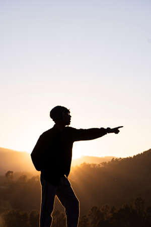 Silhouette of a young boy standing in the fields and the beautiful mountains in the background captured during sunset.の写真素材