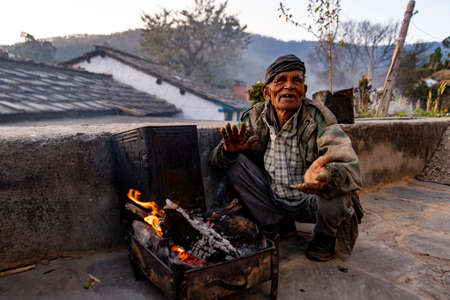 Almora, Uttarakhand - Jaunary 2 2022- An old man sitting in rugged clothes, soaking warmth from firewood. An village old man smiling into the camera.のeditorial素材