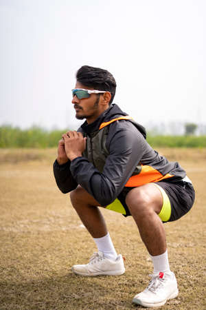 Sports and Healthy life concept - Indian young sports man with fitness clothing doing squats and...