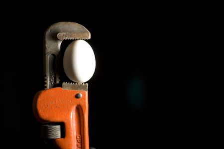 Pipe wrench holding an egg isolated on a black background.