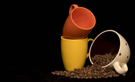 Coffee beans spread around coffee mugs on a black backgroundの写真素材