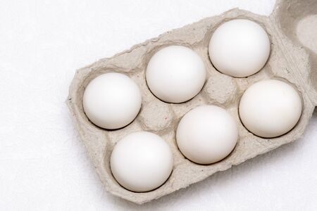 Six white eggs in a cardboard tray on a white textured background