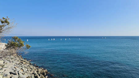 Savona, Italy - February 12, 2022: Panorama of the blue sea, light above the water, ocean sunrise. Some little waves in winter days. Clear sky reflected on the water.の写真素材