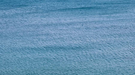 Savona, Italy - February 12, 2022: Panorama of the blue sea, light above the water, ocean sunrise. Some little waves in winter days. Clear sky reflected on the water.の写真素材