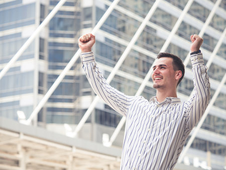 Young caucasian businessman expressing positivity celebrating success standing outdoors in the modern city, winning/winner/happy feelingの写真素材